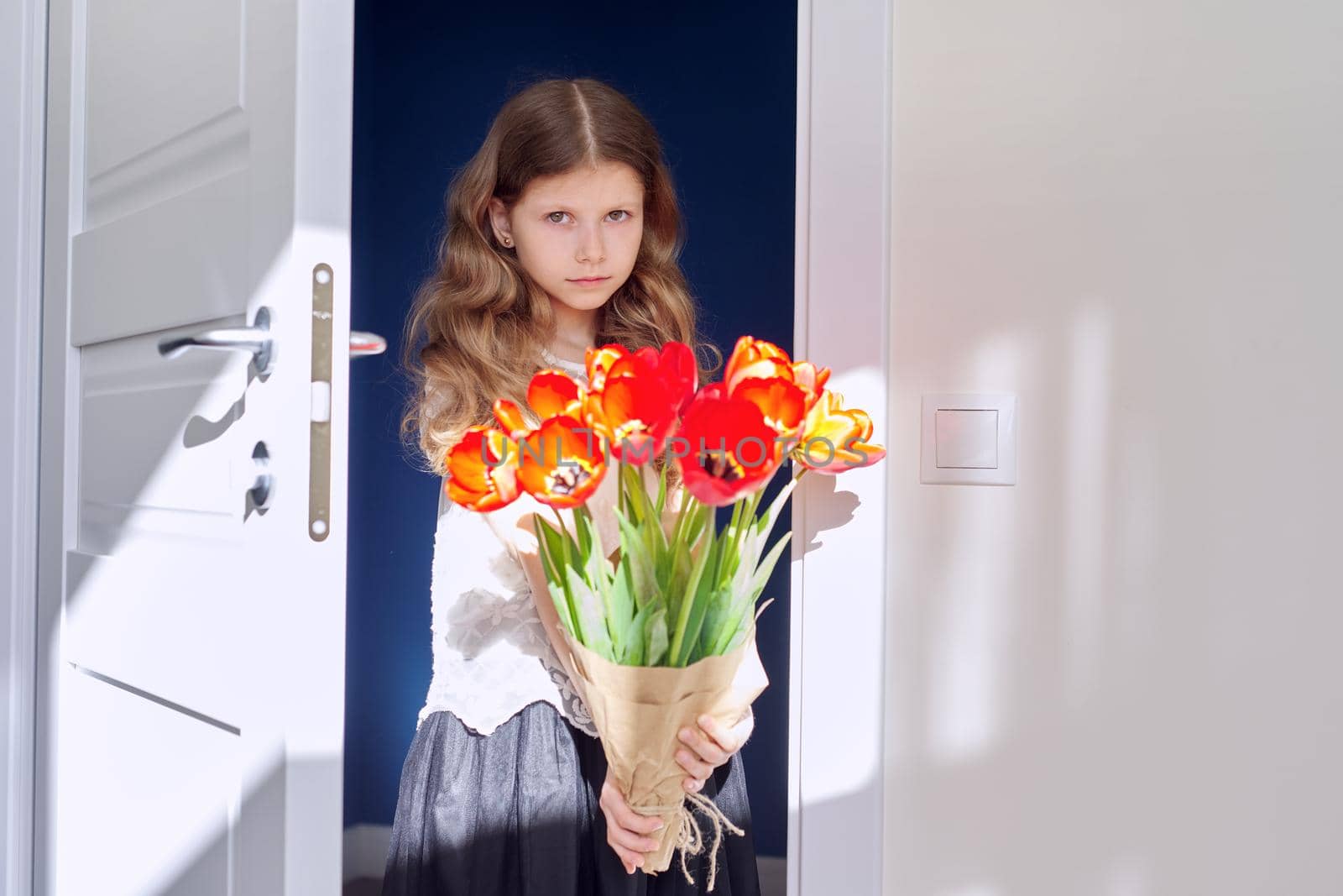 Mother's day, girl child with bouquet of red tulips flowers at home near the door. Gift for mom, love, congratulations, mom's holiday concept