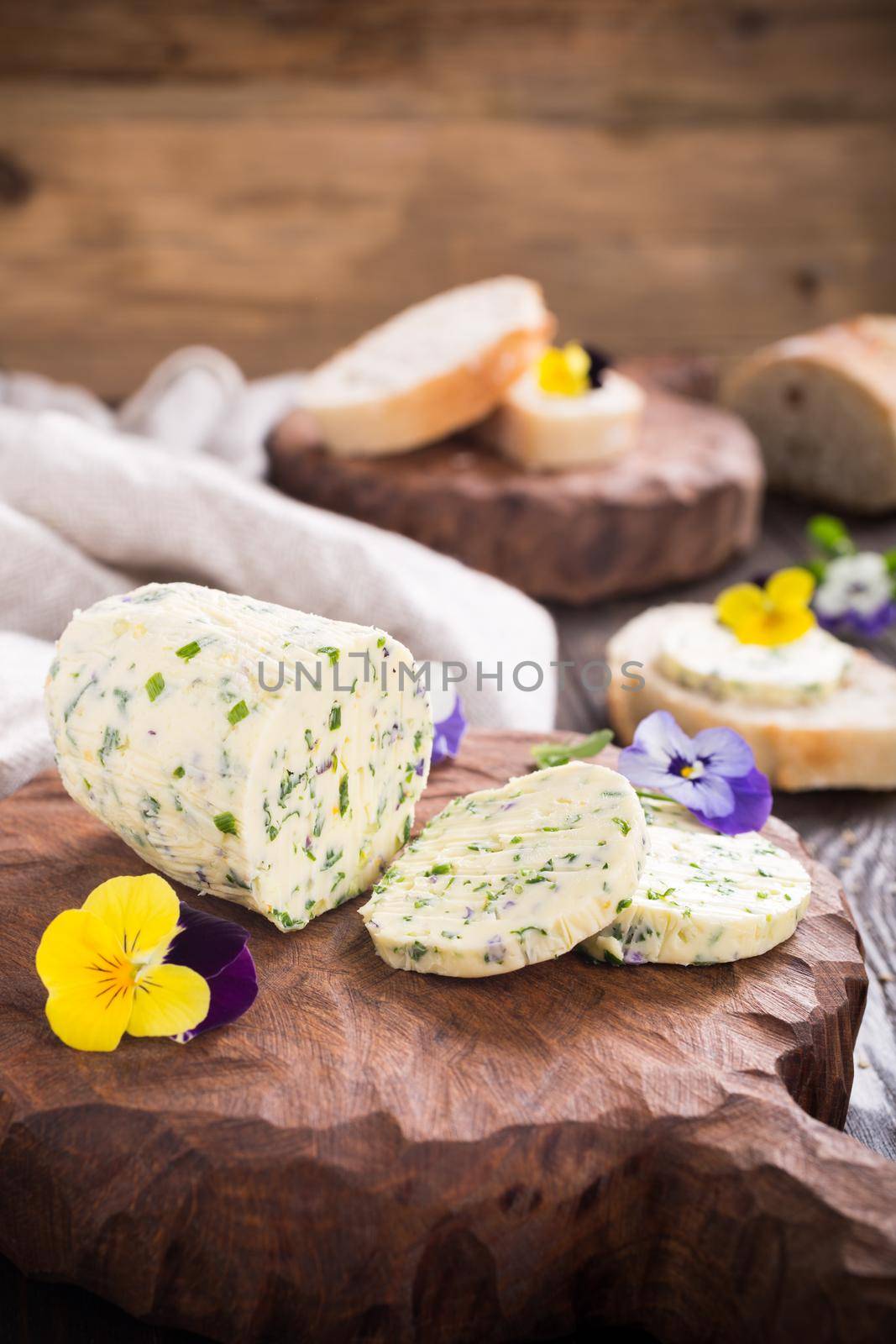 Herb butter with edible flowers on wooden cutting board, healthy food.