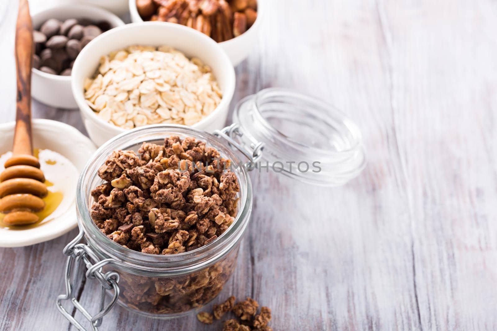 Homemade chocolate granola ingredients, nuts, oats, honey on white wooden background. Healthy breakfast concept with copy space.