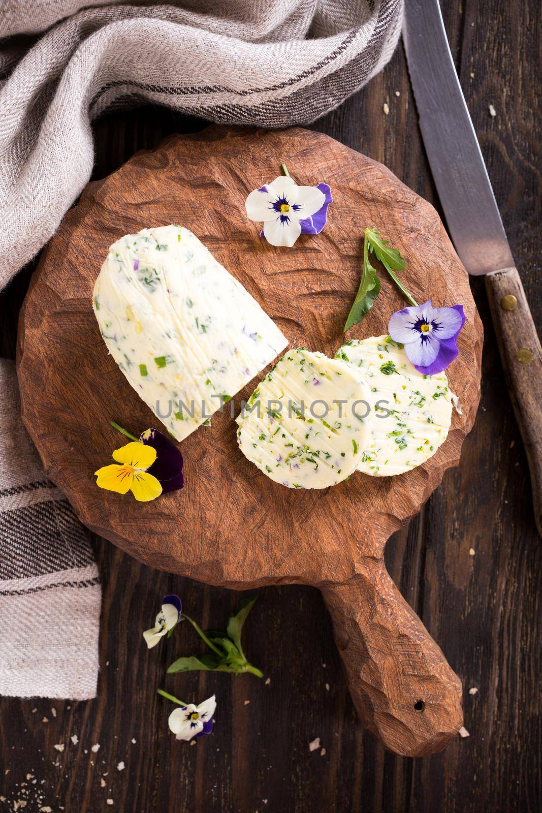 Herb butter with edible flowers on wooden cutting board, healthy food. Top view.