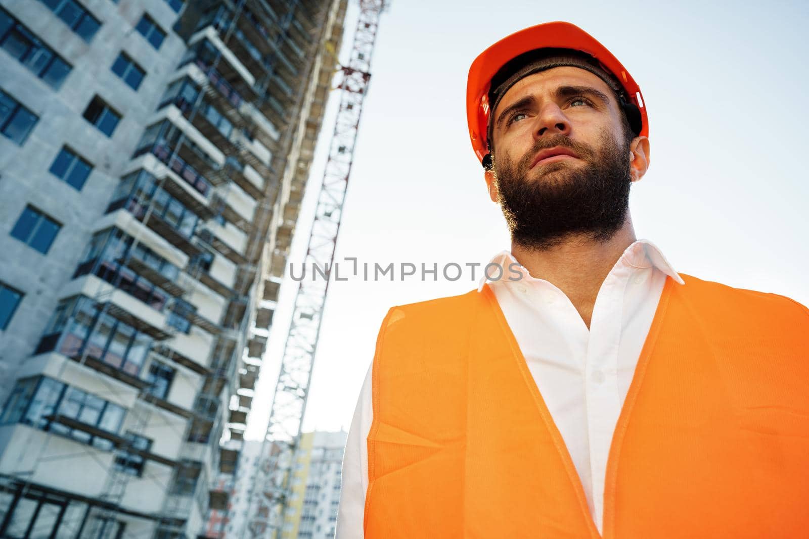 Builder wearing hardhat and safety vest standing on a commercial construction site, close up portrait