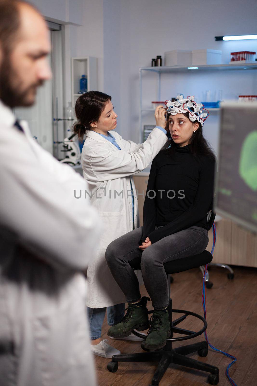 Neurologist doctor analyzing nervous system activity on monitor while specialist doctor adjusting eeg scanner of woman patient during neurology experiment. Medical team monitoring brain evolution