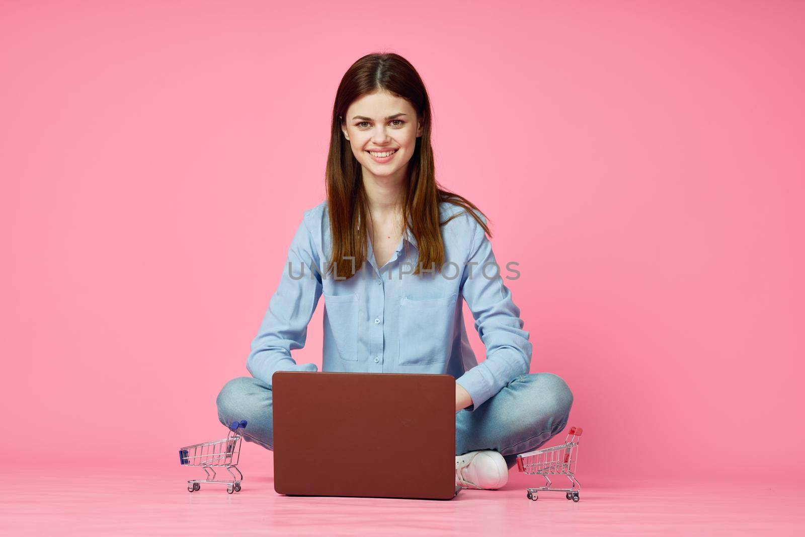 woman sitting on floor with laptop shopping entertainment pink background. High quality photo