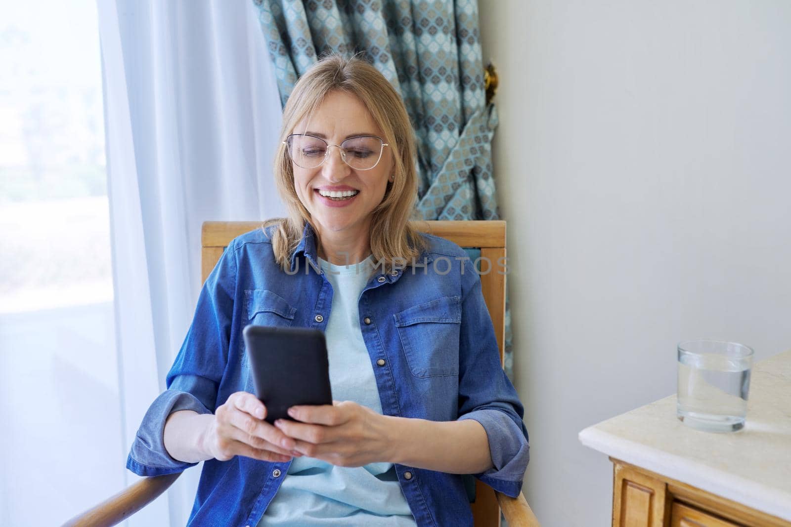 Middle aged woman looking at smartphone screen smiling talking by VH-studio