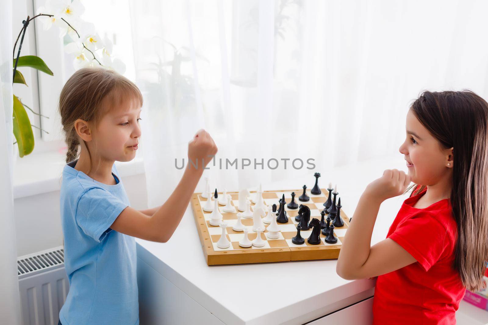 Two little sister playing chess at home by Andelov13