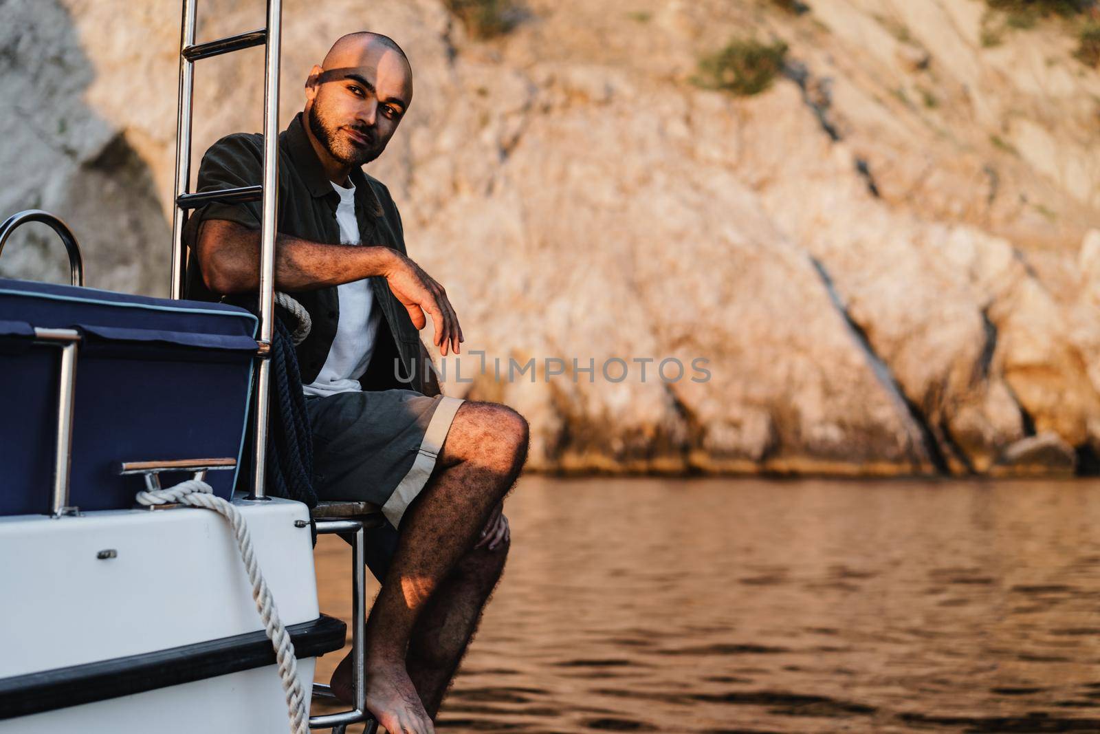 Young african american man relaxing on a sailboat in open sea at sunset by Fabrikasimf