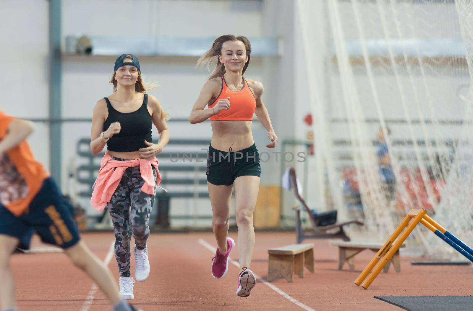Two young athletic women running in sports arena indoors. Mid shot