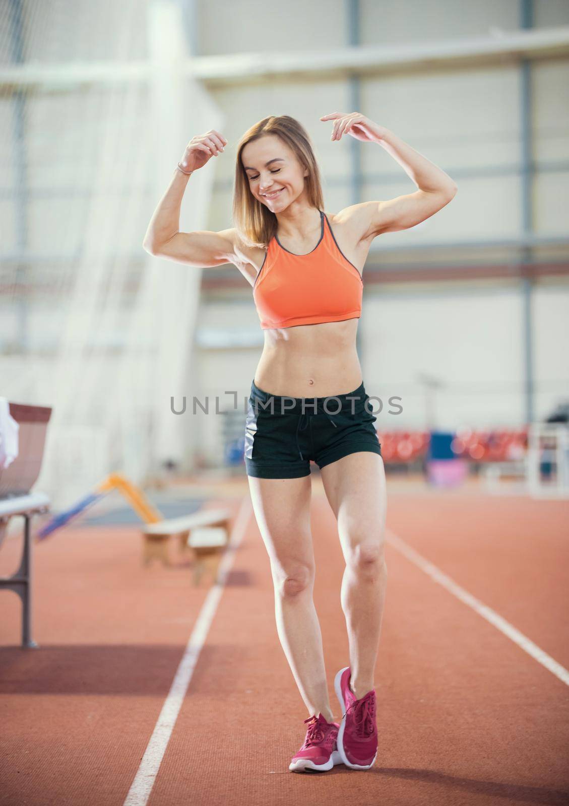 Young healthy woman in a good shape in sport shorts posing for the camera showing her muscles. Smiling. Full height