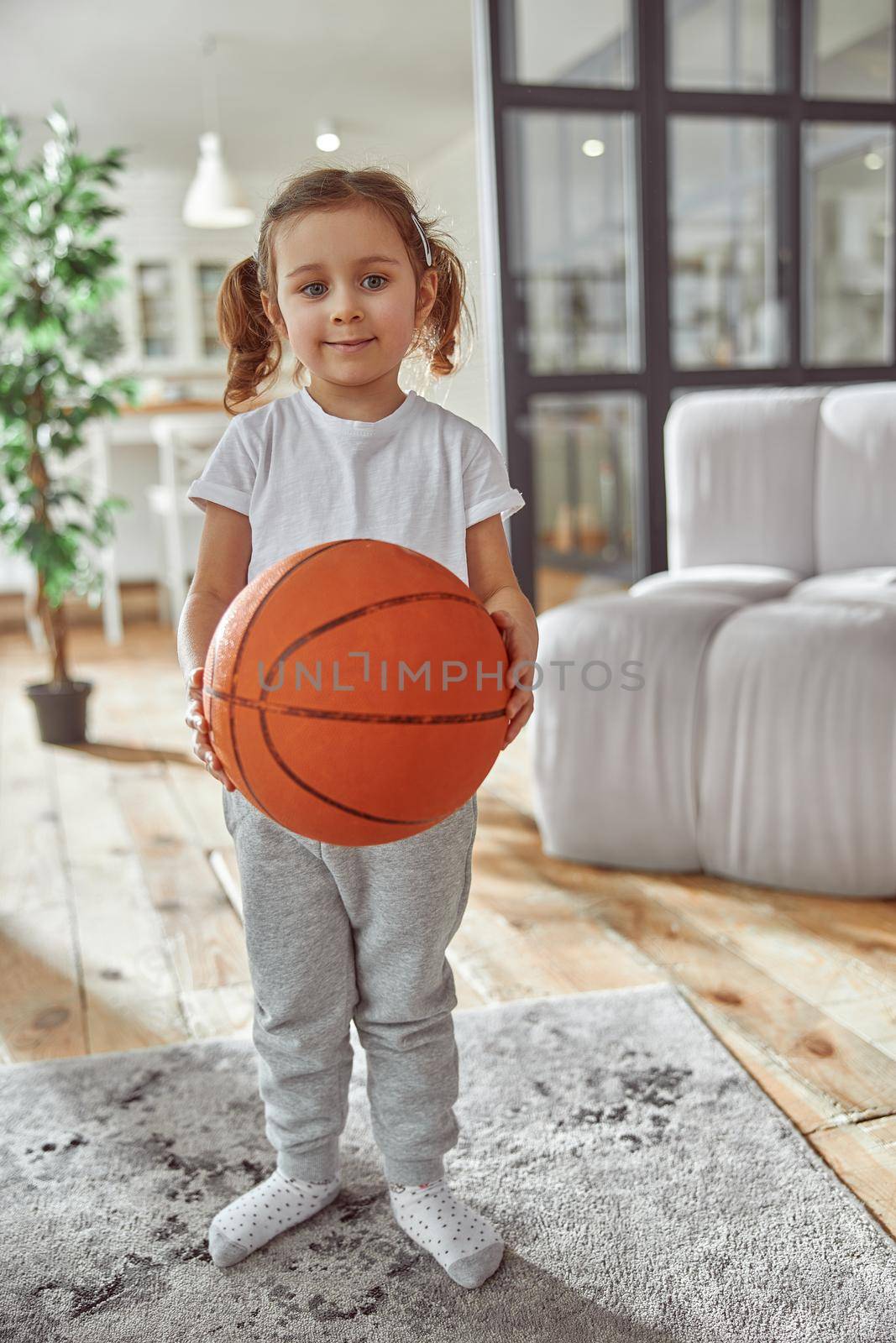 Full length portrait of smiling little lady standing at home and holding sport ball for game