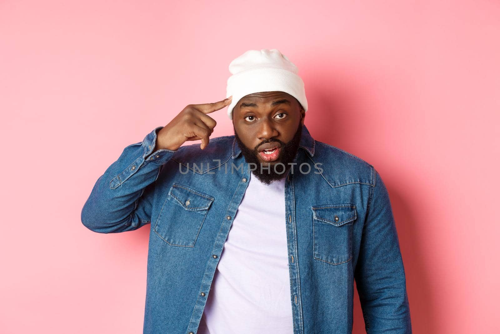 Annoyed and pissed-off african-american man pointing finger at head, scolding someone stupid, staring bothered at camera, pink background.