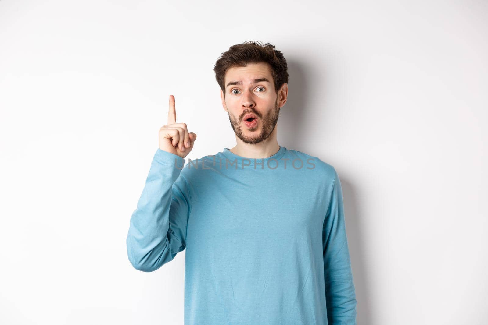 Image of excited handsome man pitching an idea, raising finger and saying eureka, standing over white background.