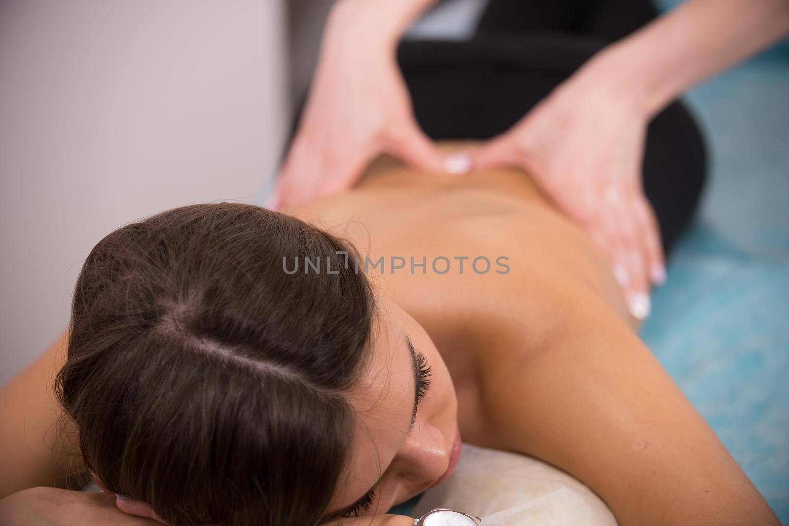 Masseur doing a back massage to a young slim woman with tanned skin with closed eyes at the clinic, her head and shoulder in the front view