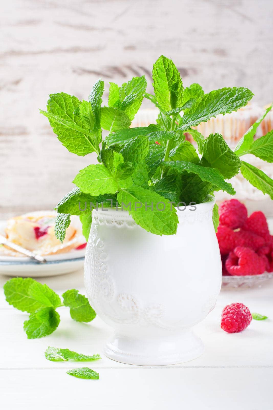 Fresh mint in white vase for decorating desserts on white wooden background. Selective focus.