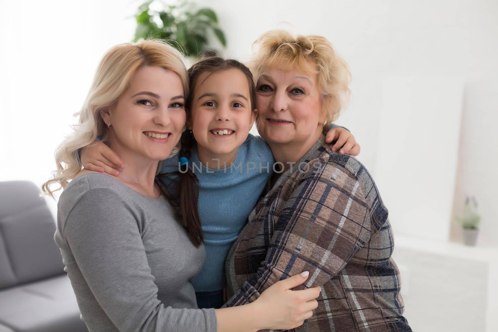 Three generations of women. Beautiful woman and teenage girl are kissing their granny while sitting on couch at home