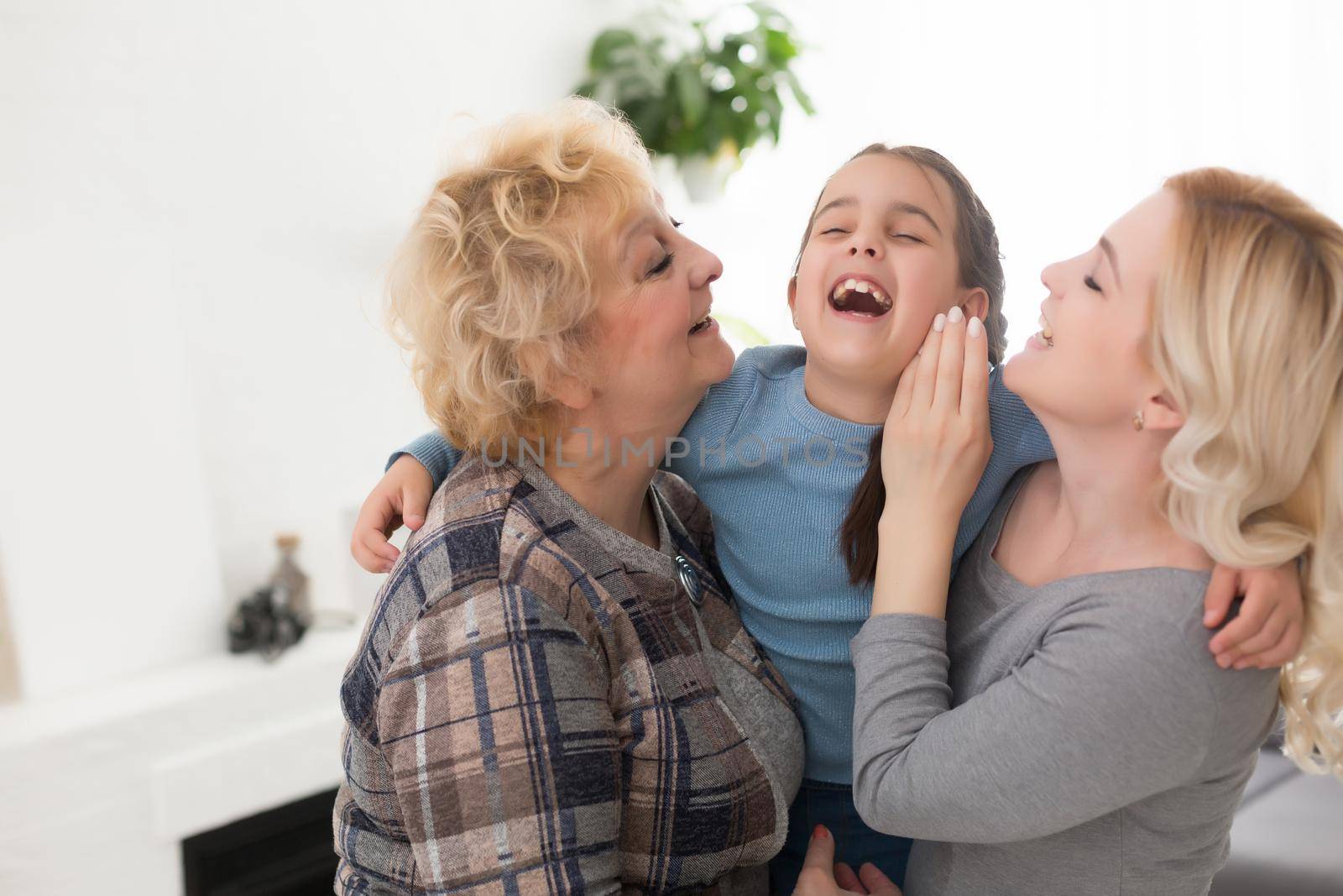 Three generations of women. Beautiful woman and teenage girl are kissing their granny while sitting on couch at home