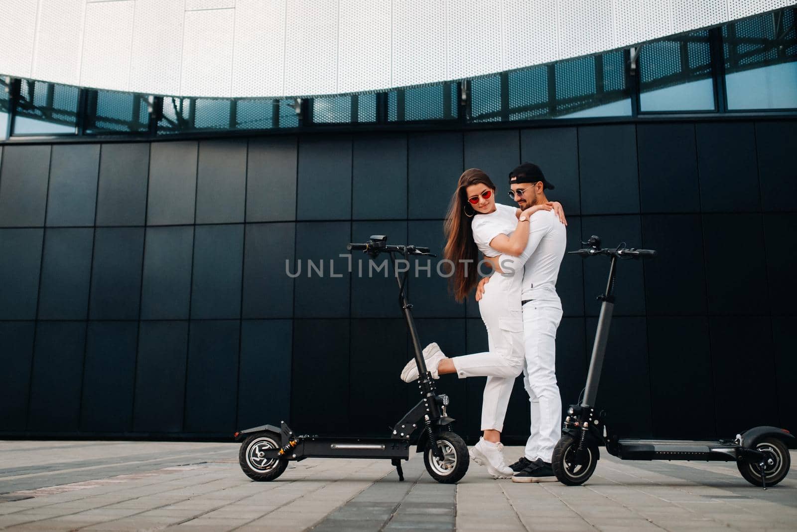 A girl and a guy are walking on electric scooters around the city, a couple in love on scooters