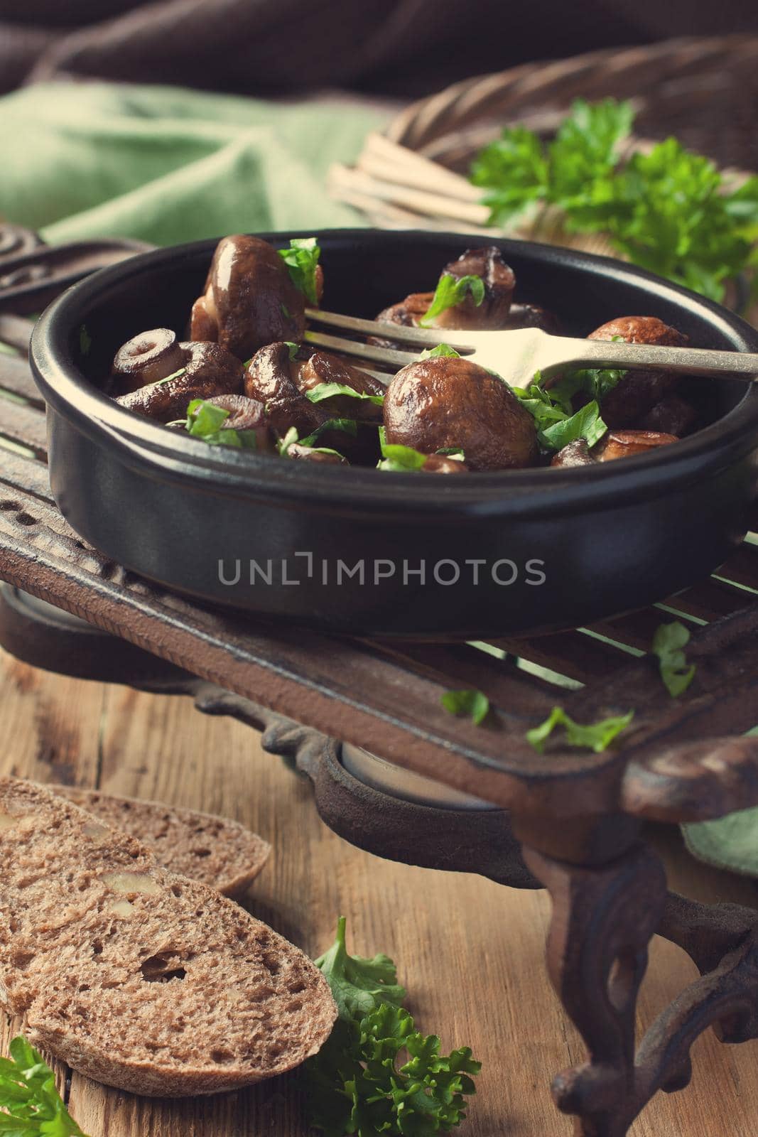 Baked champignons mushrooms with butter, parsley and roasted garlic in black bowl. Selective focus. Healthy food concept. Retro style toned.