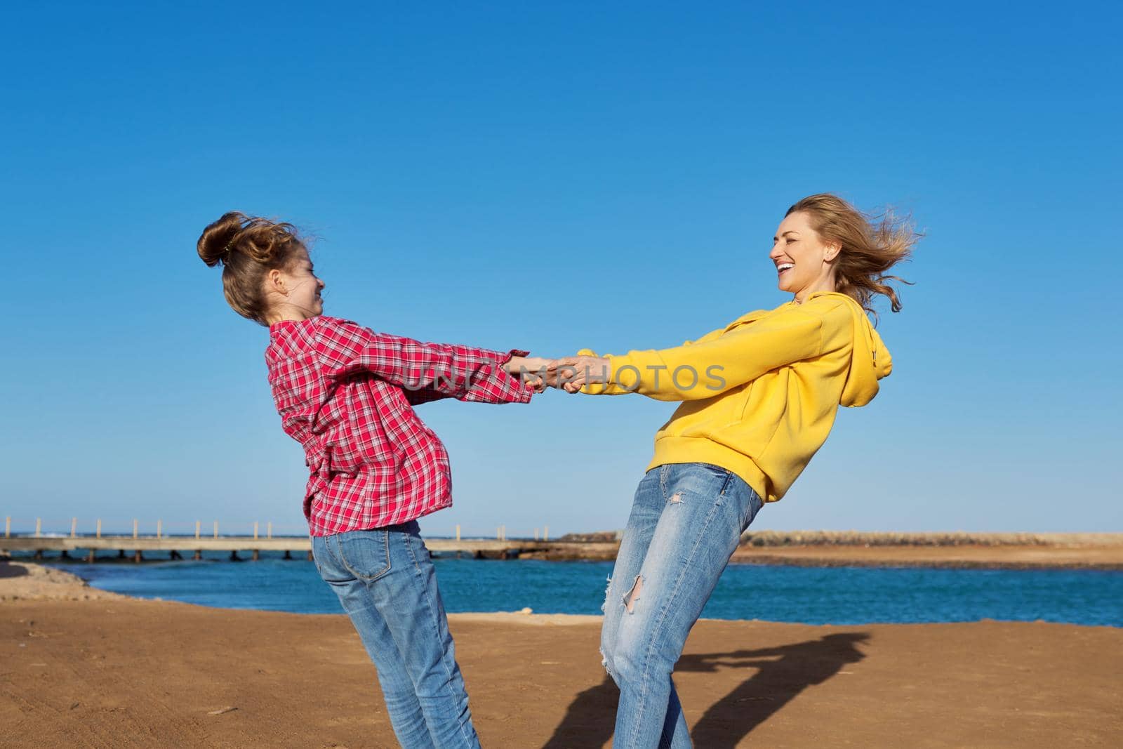 Happy mom and daughter child have fun together on the sea beach. Blue sky background, family, love, happiness, joy, childhood concept