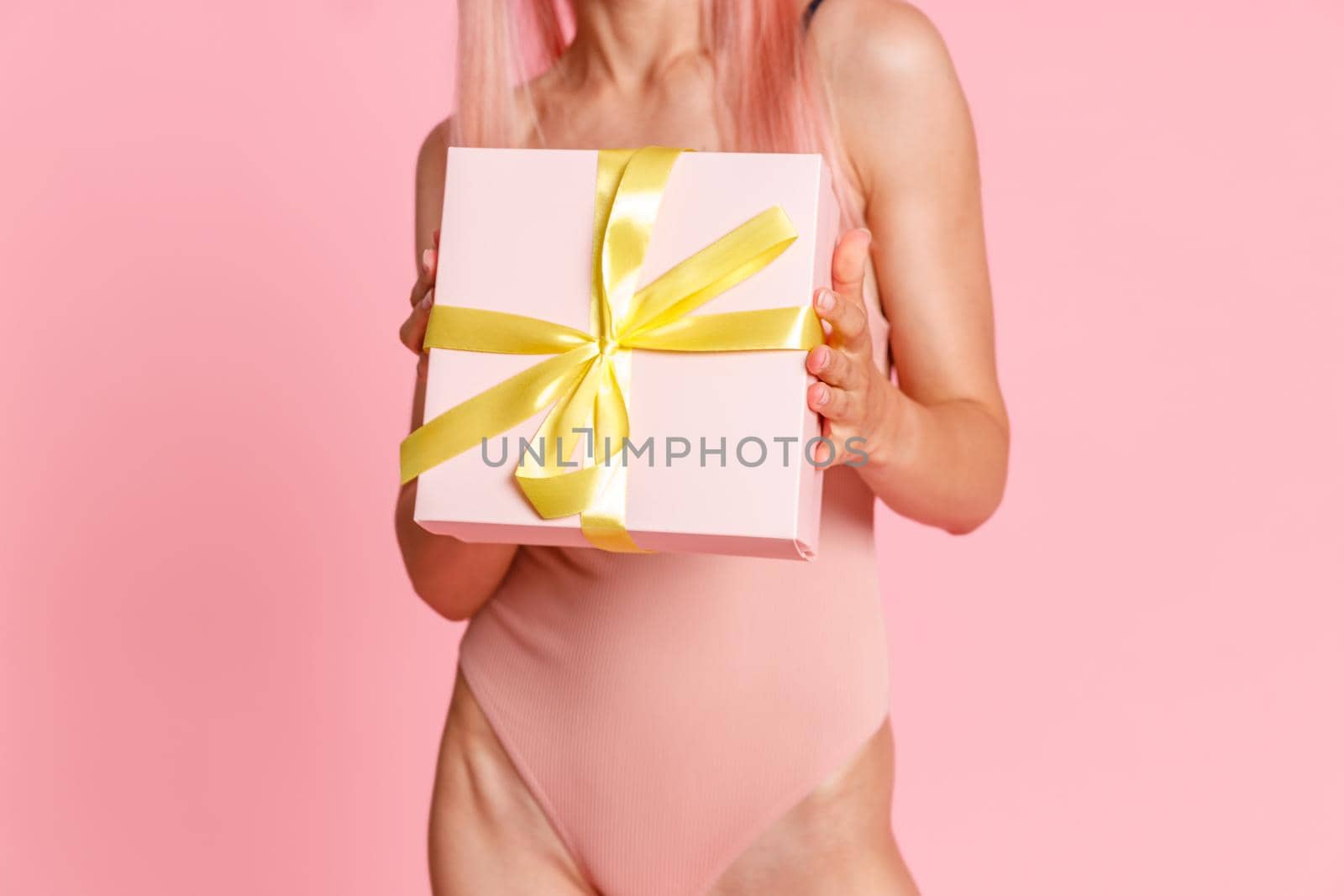 Close up shot of woman in swimsuit holding cute gift box, standing isolated over pink background by Yaroslav_astakhov