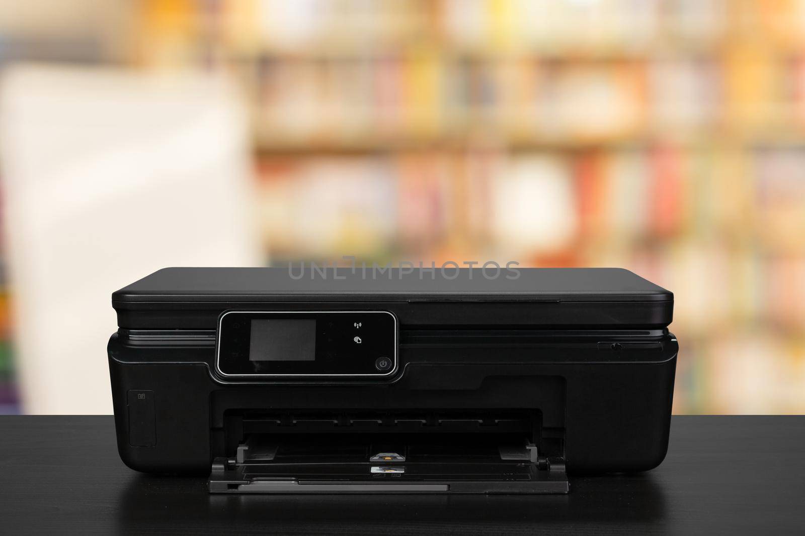 Compact laser printer on black desk against blurred background, close up