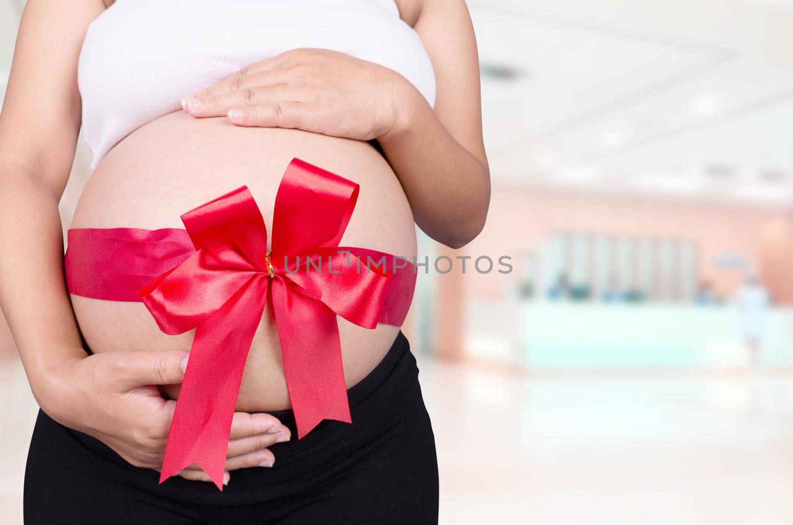 close up pregnant woman with red ribbon gift on belly in hospital background