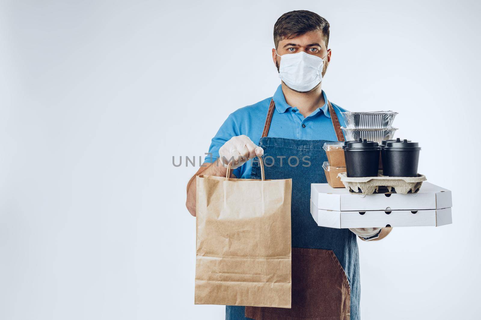 Delivery man in protective mask and medical gloves holding takeaway food. Compliance with the hygiene rules while covid-19 pandemic by Fabrikasimf