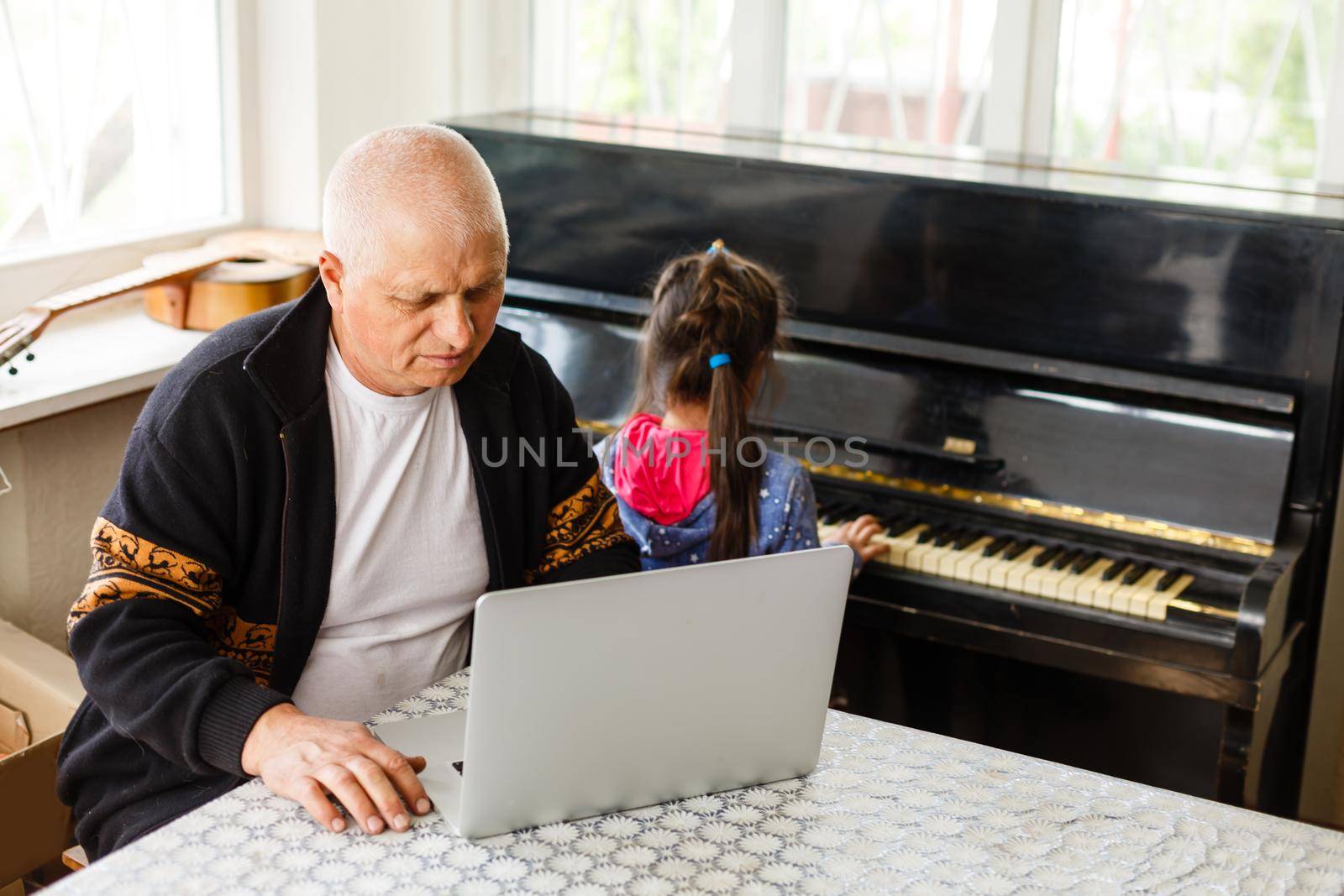 little girl plays piano together with grandfather, learning online on a laptop by Andelov13