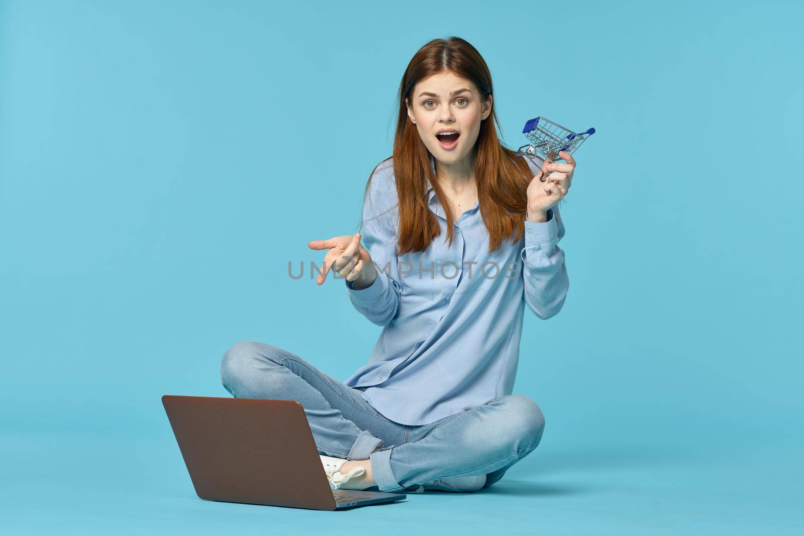 woman with laptop sitting on the floor learning student technology blue background. High quality photo