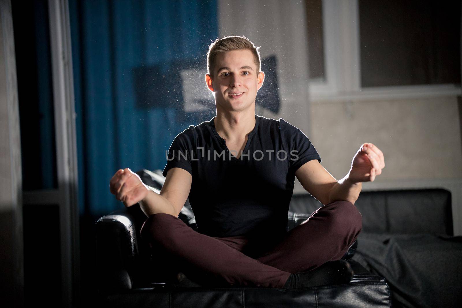 Young attractive smiling guy sitting in lotus pose. Portrait
