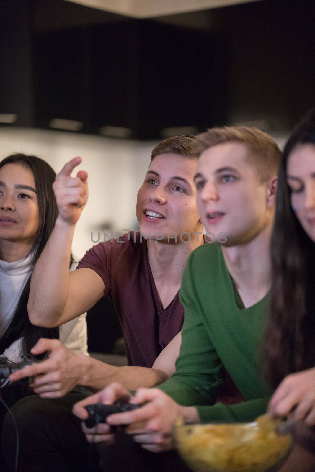 Young friends sitting on the sofa. Young men holding a joystick and women eating chips. Mid shot