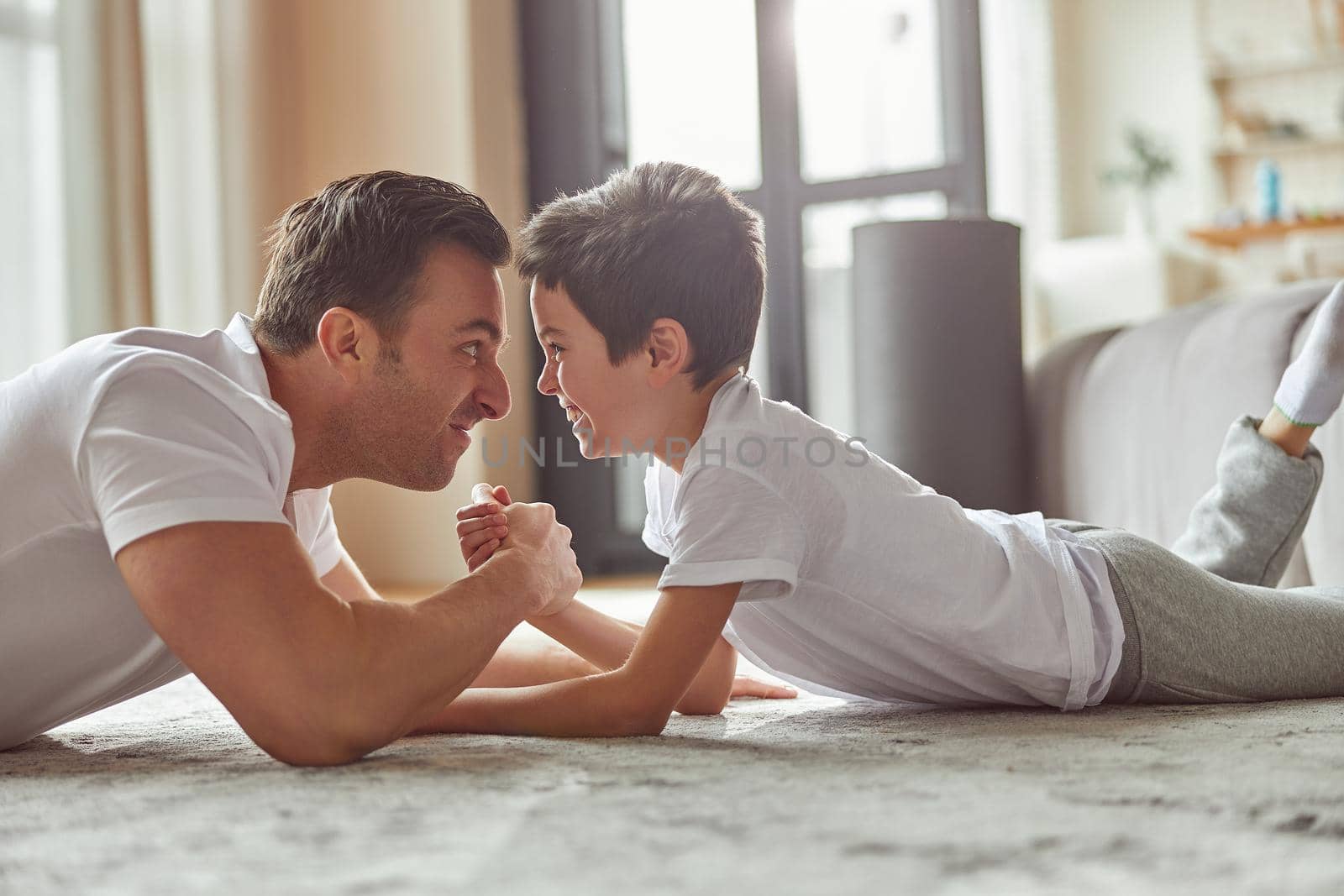 Merry man is fighting hands with little boy while having fun on floor in living room