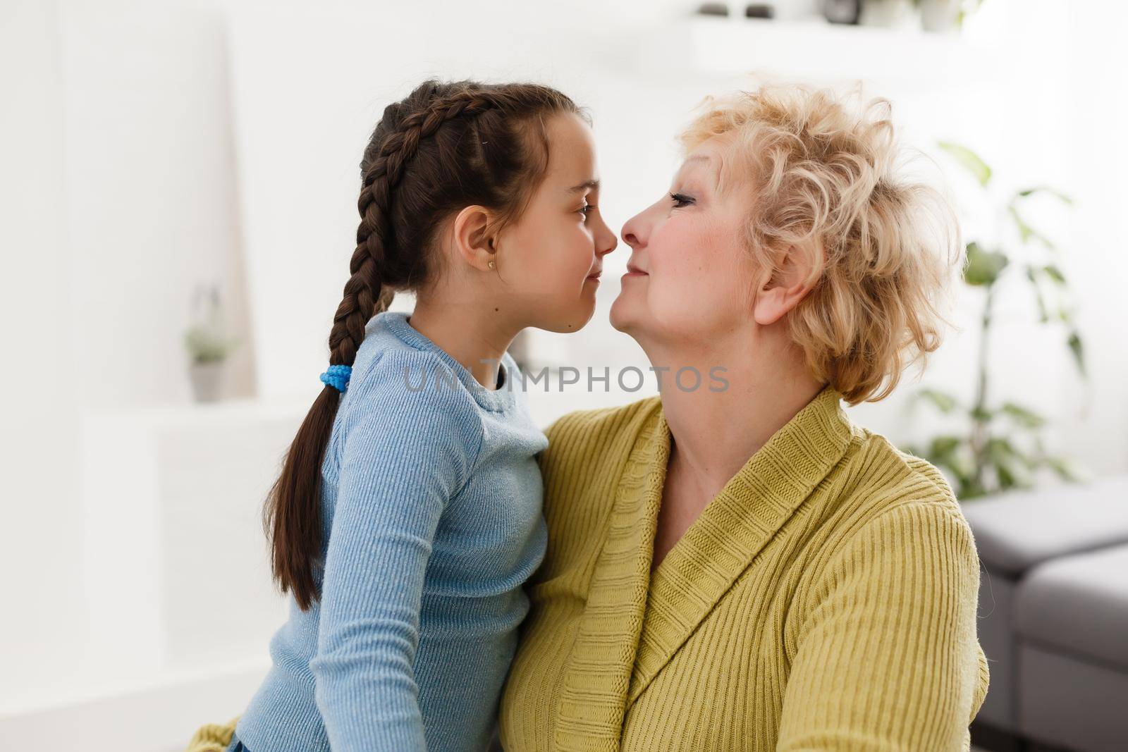 Little granddaughter and happy grandmother giving high five having fun playing together sitting on sofa, smiling grandma granny and preschool grandchild laughing celebrating good relations at home