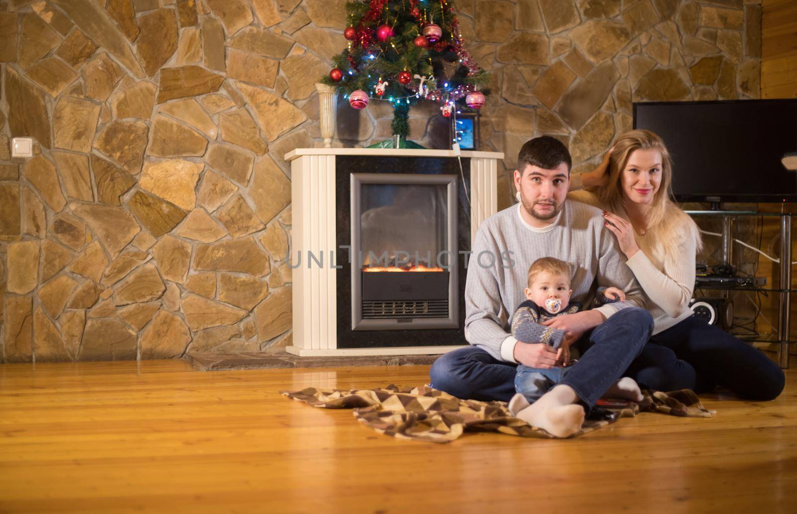 Young family sitting in on the floor in cozy house. Parents and a baby. Mid shot