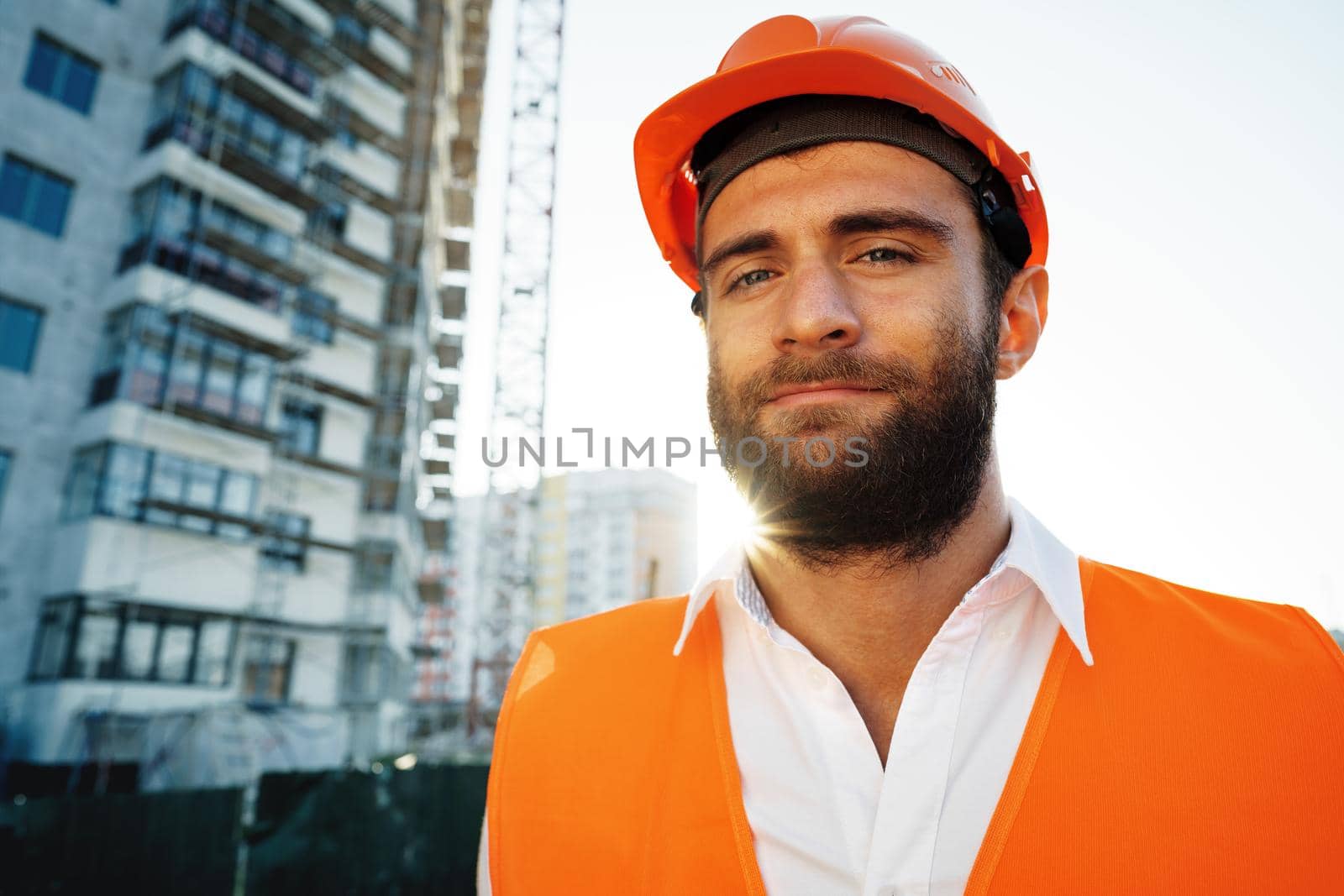 Builder wearing hardhat and safety vest standing on a commercial construction site, close up portrait