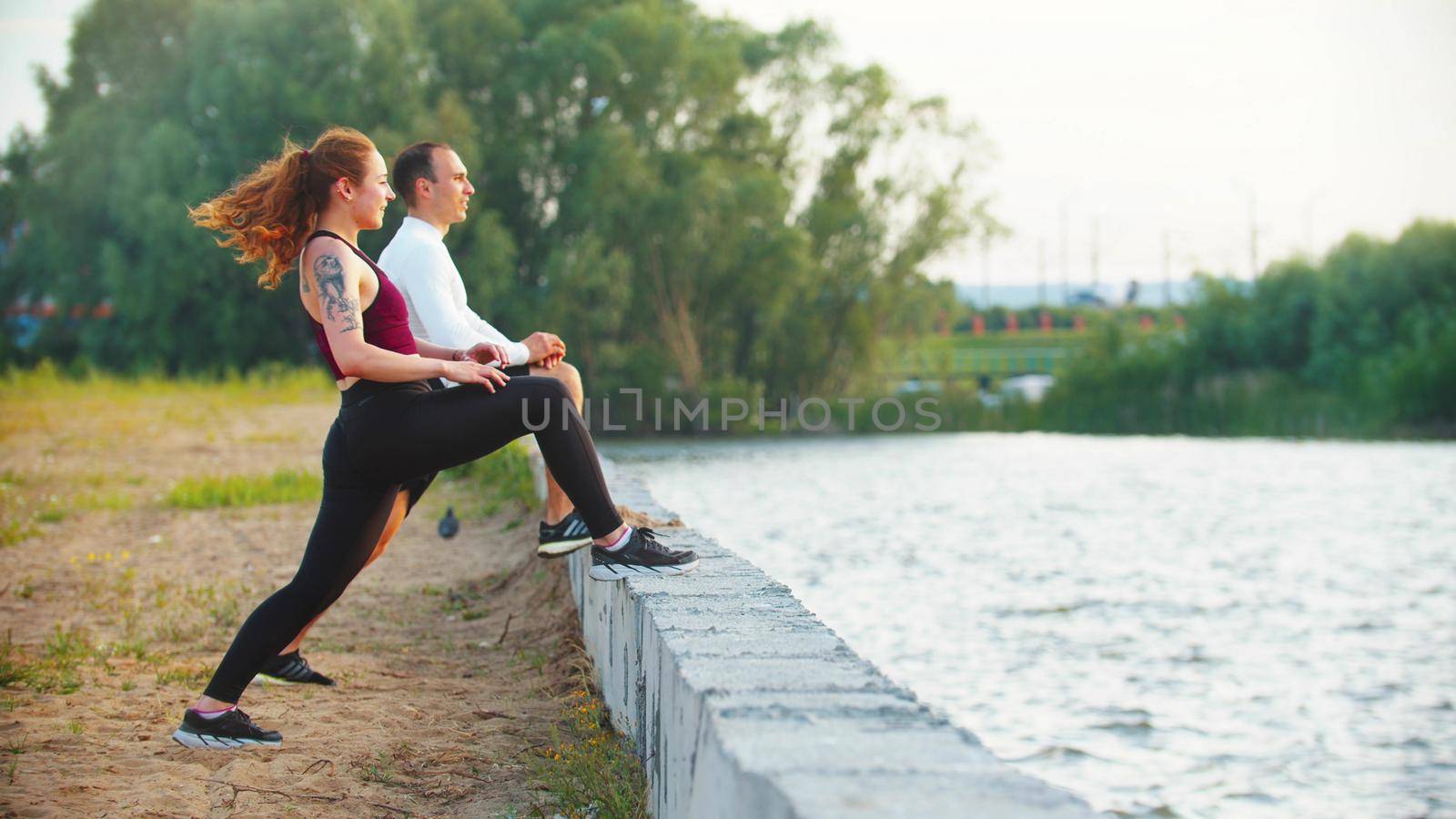 Man and woman stretching leg muscles resting their feet standing near the waterfront by Studia72