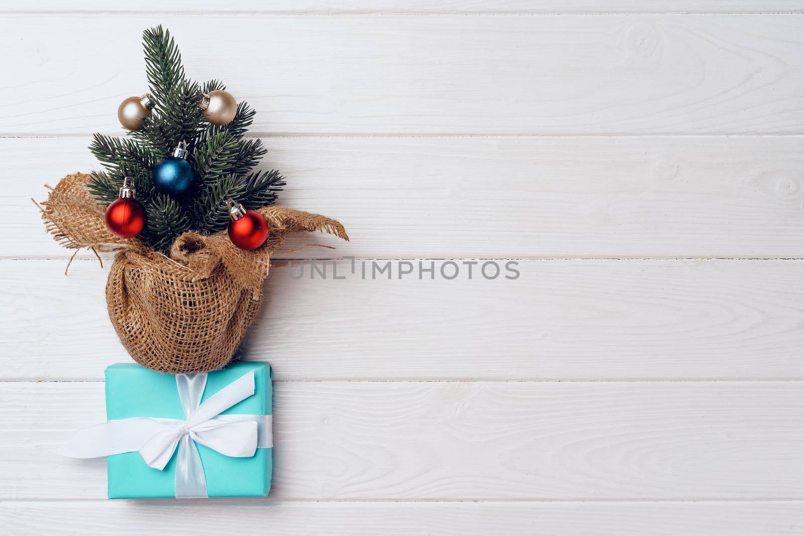 Pine tree decorated with baubles and wrapped Christmas gifts on white wooden background top view