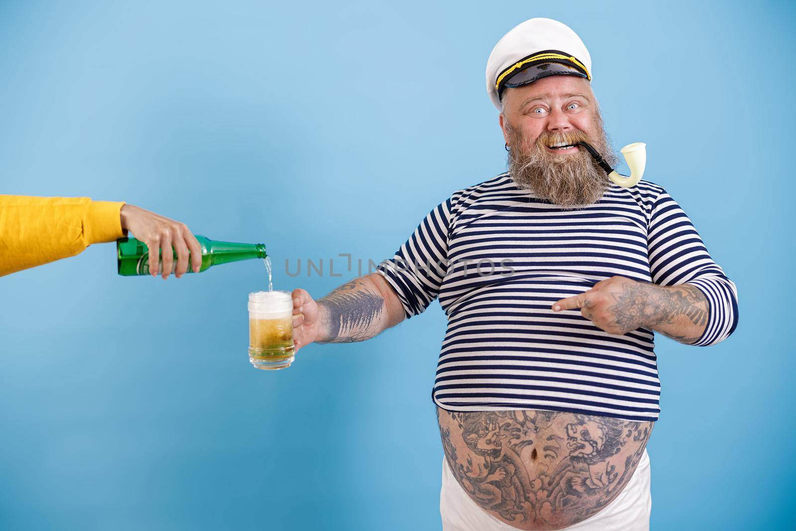 Cheerful sailor with overweight holds mug while woman pours beer on light blue background by Yaroslav_astakhov