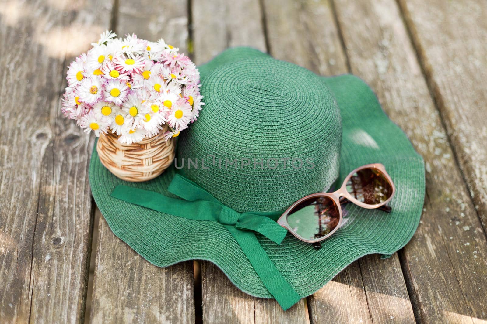 daisies lying on a green hat near sunglasses. Designer old-fashioned floristics bouquet of meadow and wild flowers. A romantic photo of a cute spring bouquet. hat with bouquet of daisies. summer vacation concept