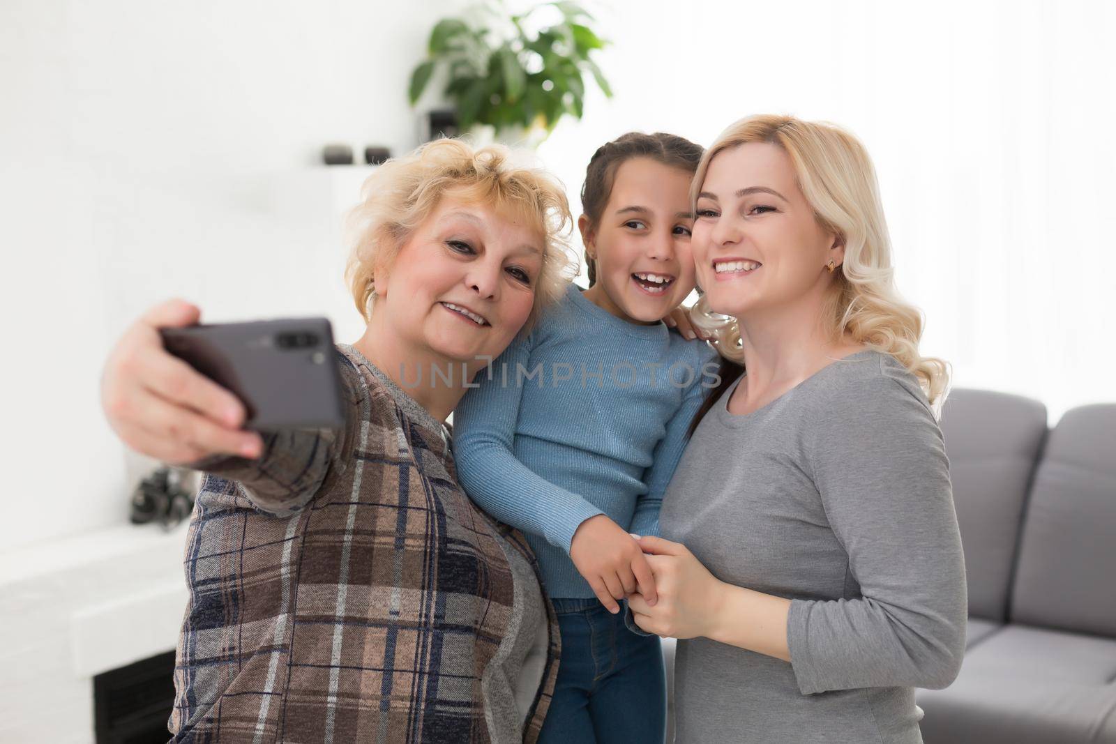 Three generations of women. Beautiful woman and teenage girl are kissing their granny while sitting on couch at home