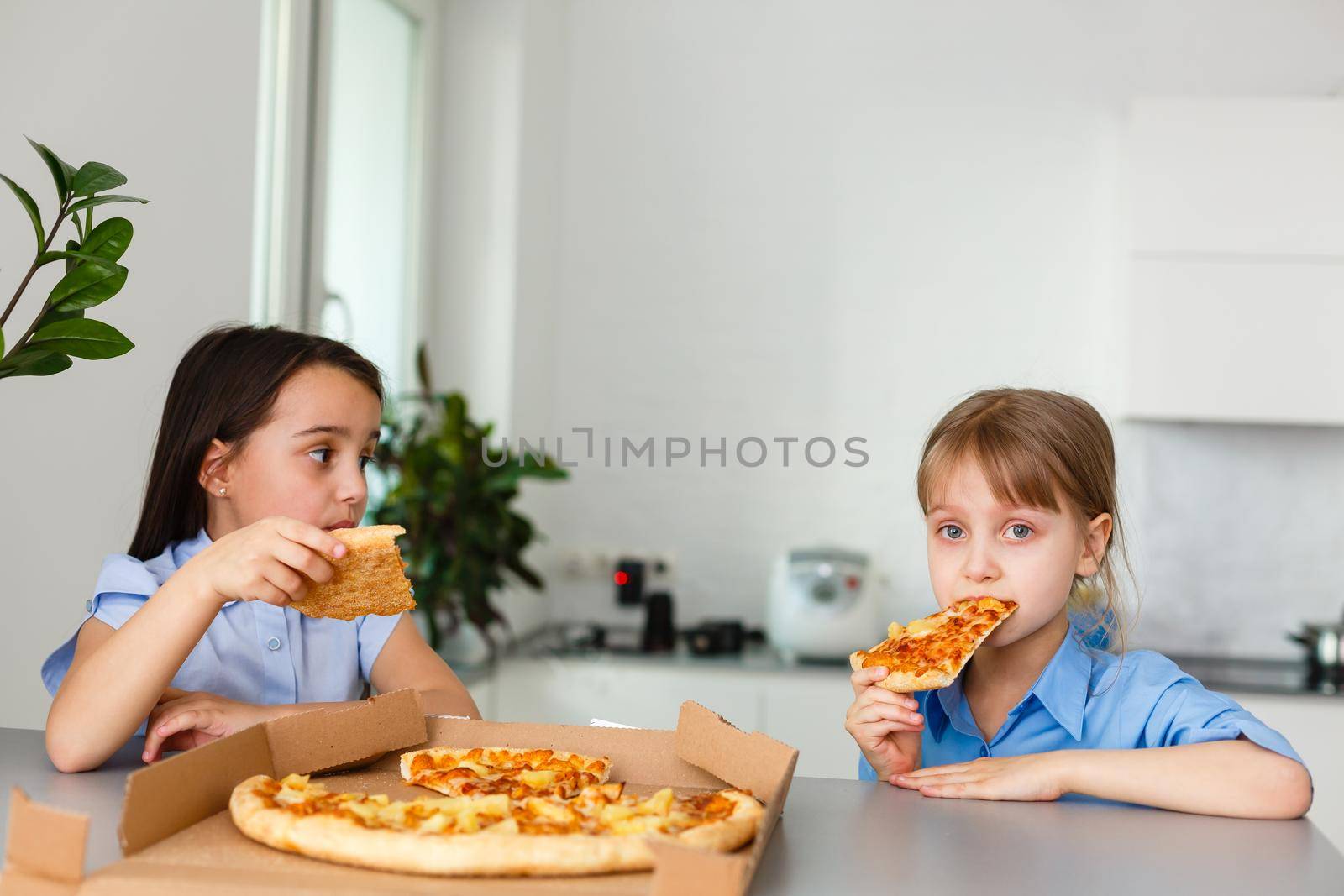 Two happy little child girl friends eating pizza slices.