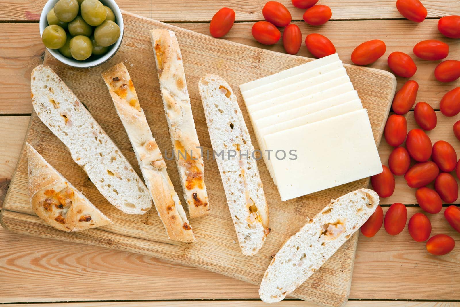 Fresh whole grain bread with cheese and green olives and tomatoes. Natural food concept. Loaf of organic bread on wooden background.