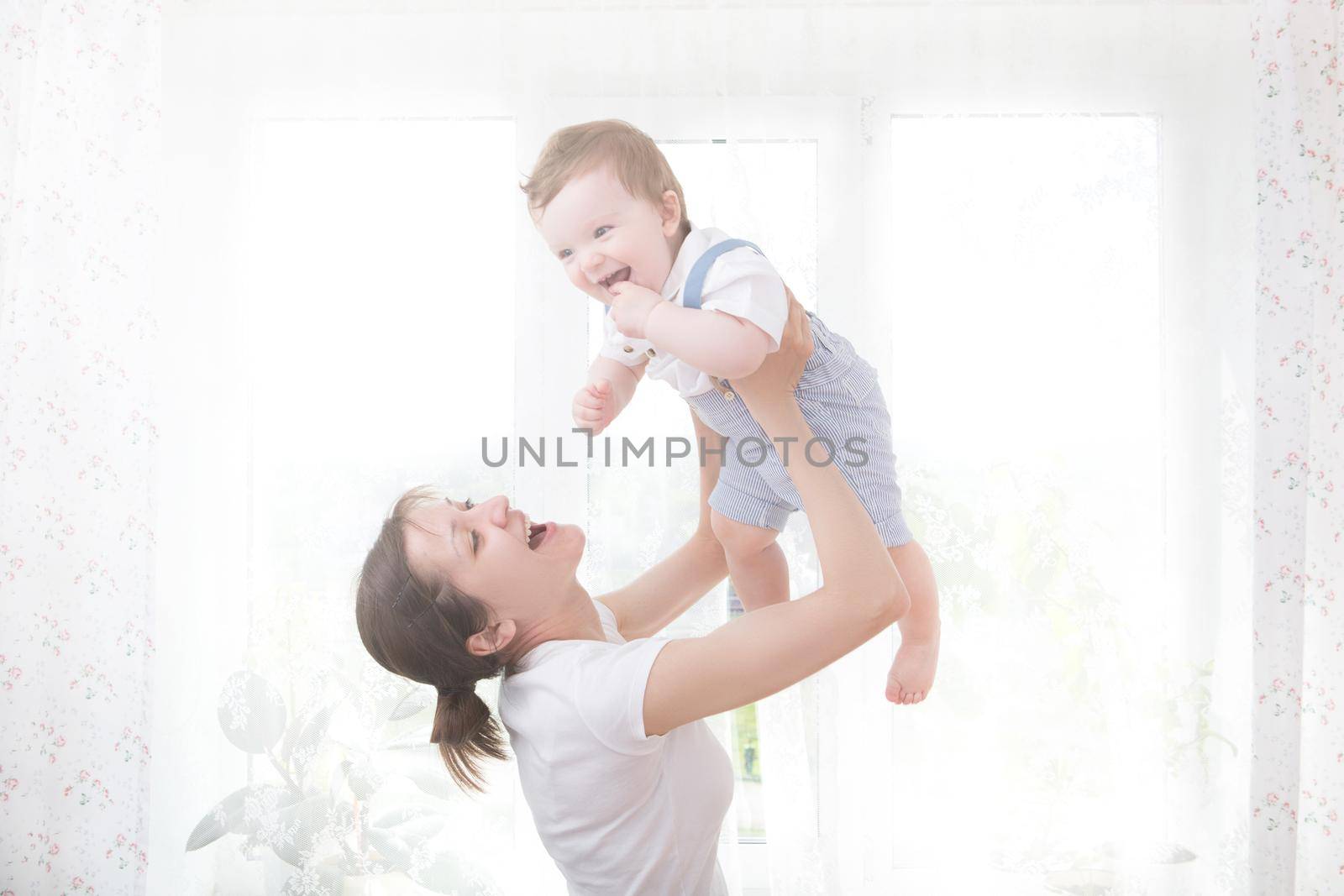 Young mother holding her newborn child. Mom nursing baby. Woman and new born boy relax in a white bedroom. Nursery interior. Mother breast feeding baby. Family at home