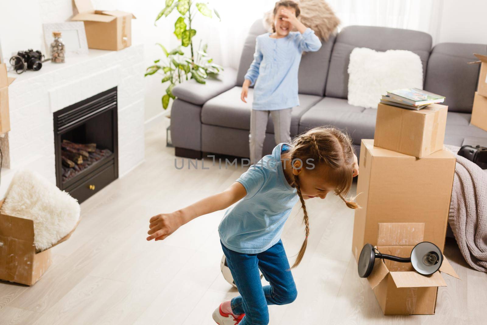 two little daughters celebrating moving day, excited by relocation into new house, laughing living room with cardboard boxes