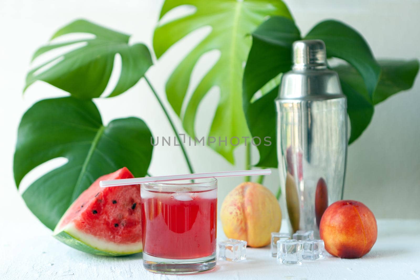 watermelon smoothie on the white board. Delicious Smoothie - vegetarian coctail from fresh fruit with peach and ice. watermelon summer cocktail infront of monstera tropical plant