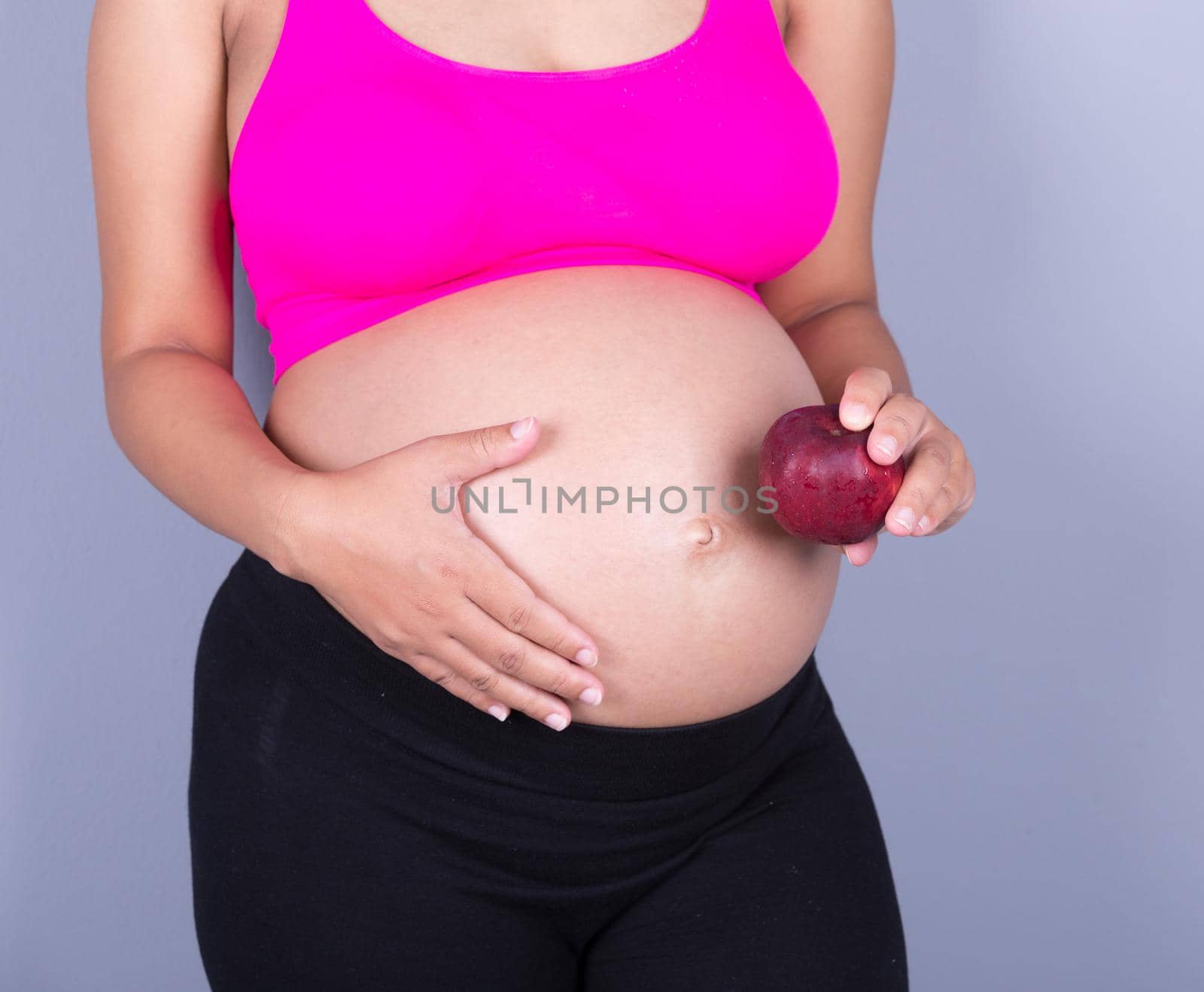 close-up belly of pregnant woman with red apple on gray background by geargodz