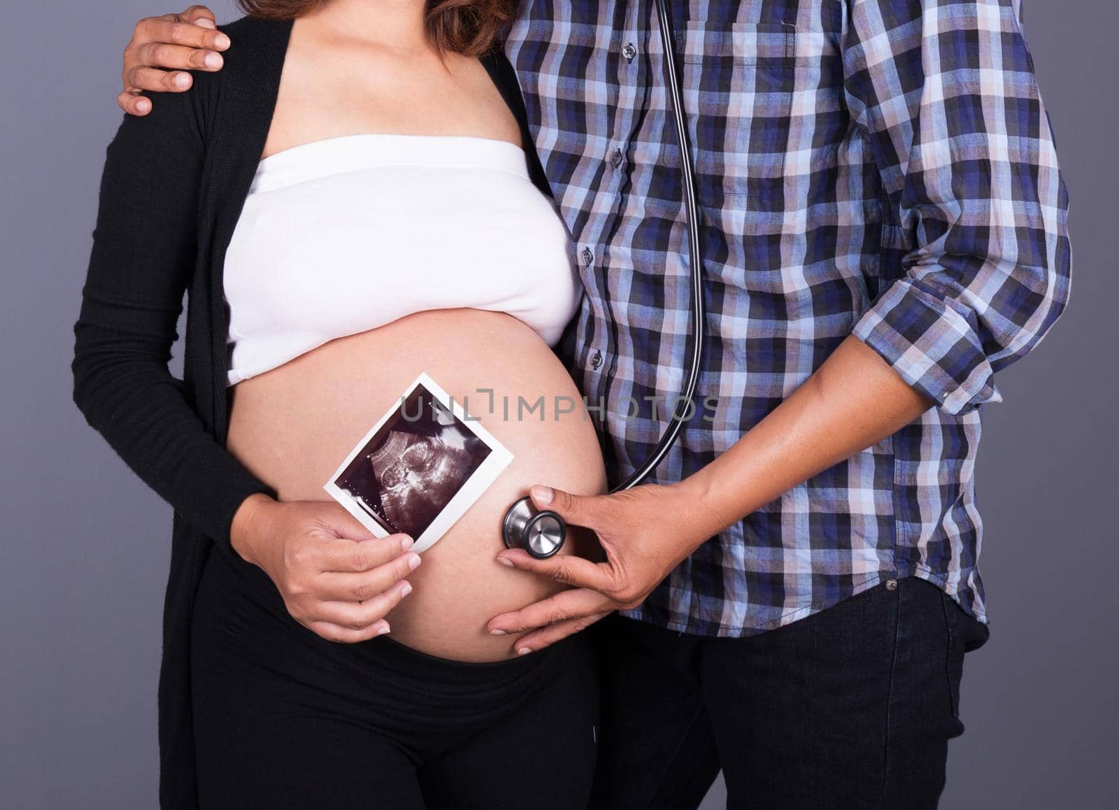 close up pregnant and husband with stethoscope and ultrasound image on gray wall background