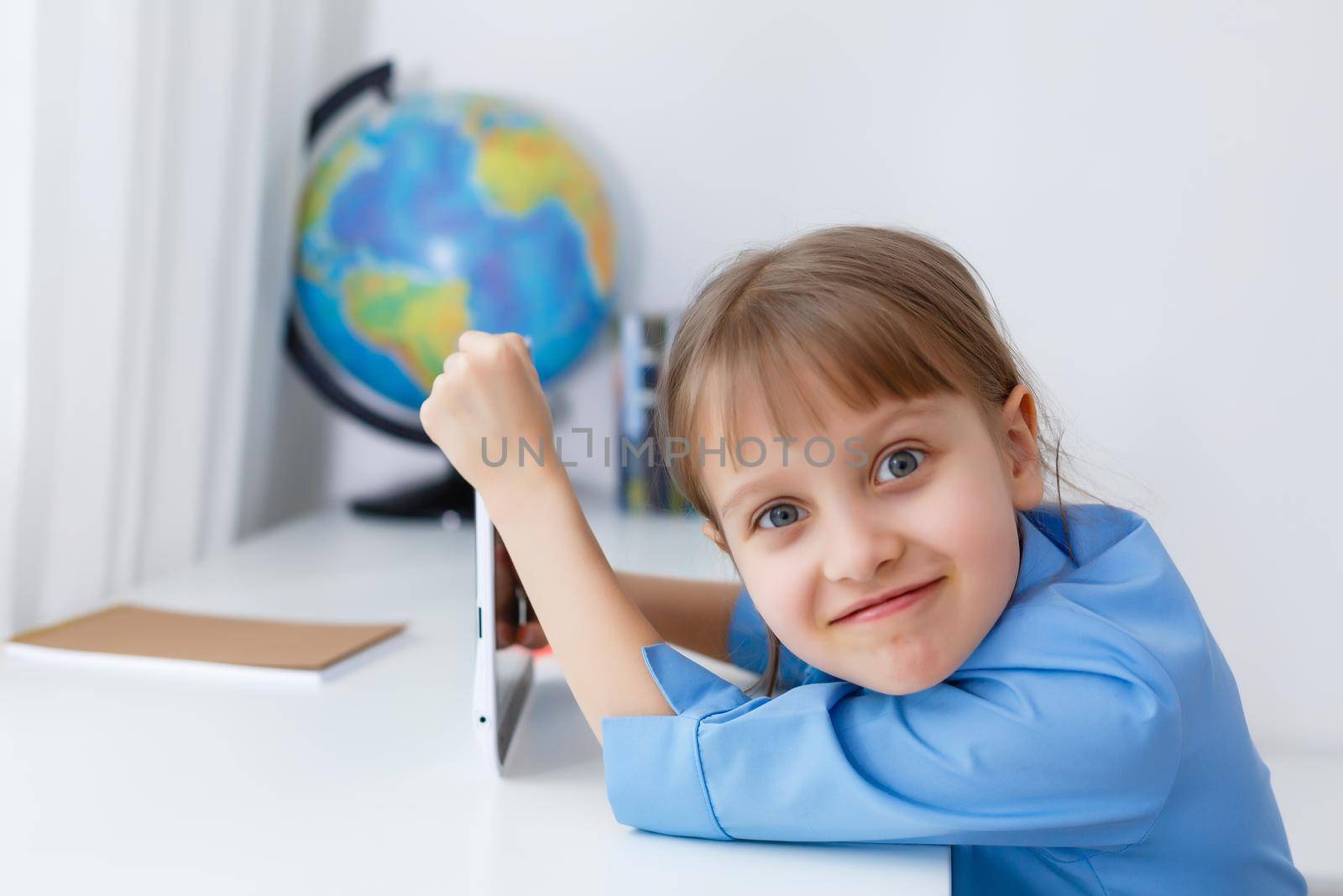 Cute little girl is sitting at table with her laptop and studying online