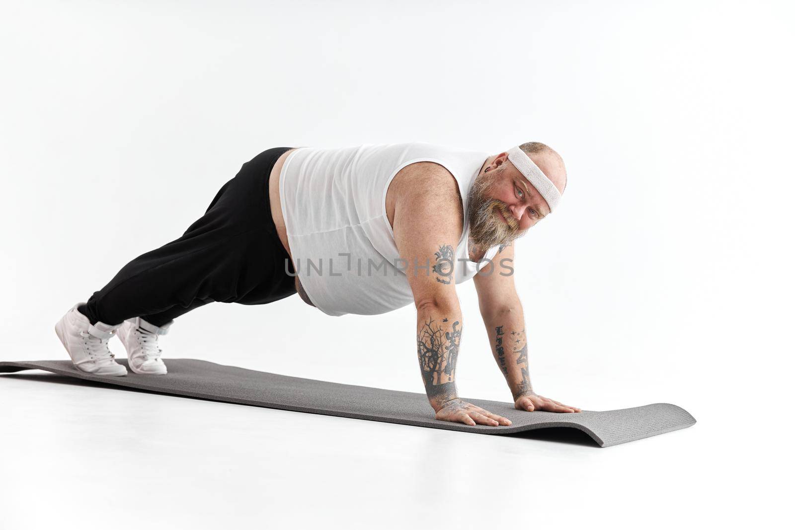 Sporty fat man with beard and tattoos is doing yoga