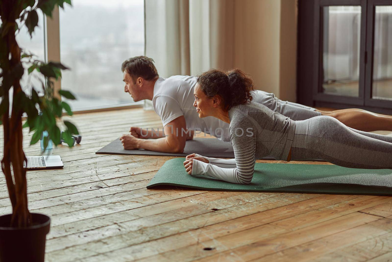 Sporty couple doing plank before laptop indoors by Yaroslav_astakhov