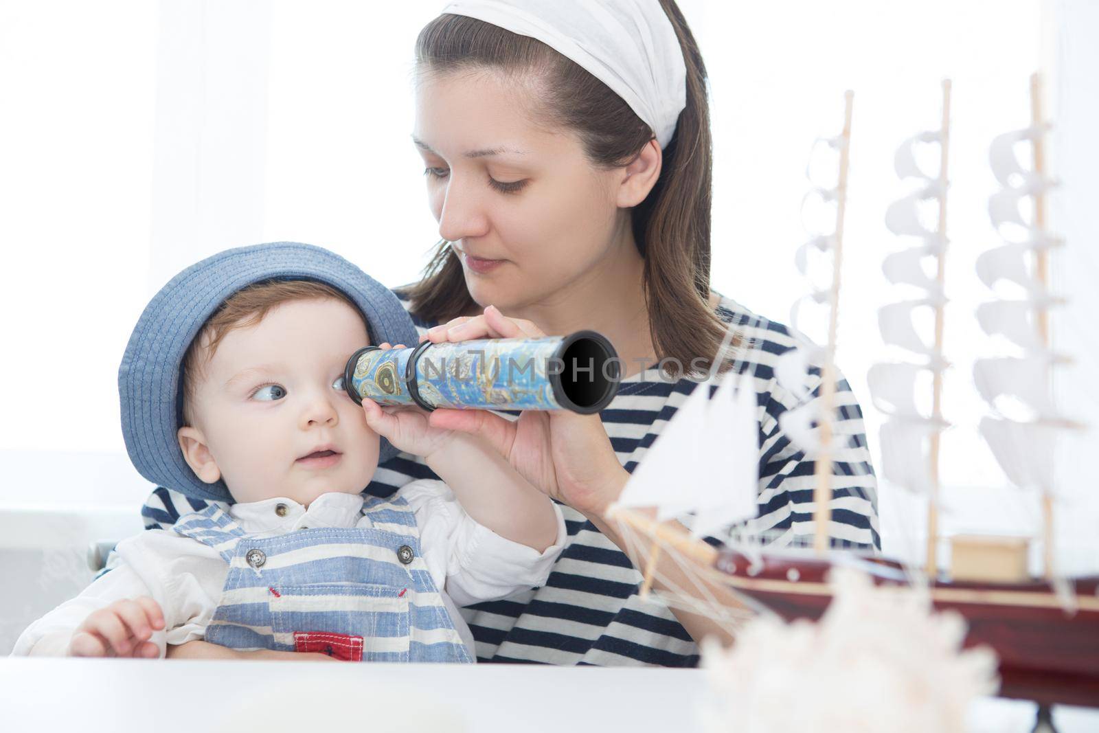 Happy kid and mom playing with toy sailing boat indoors. Travel and adventure concept